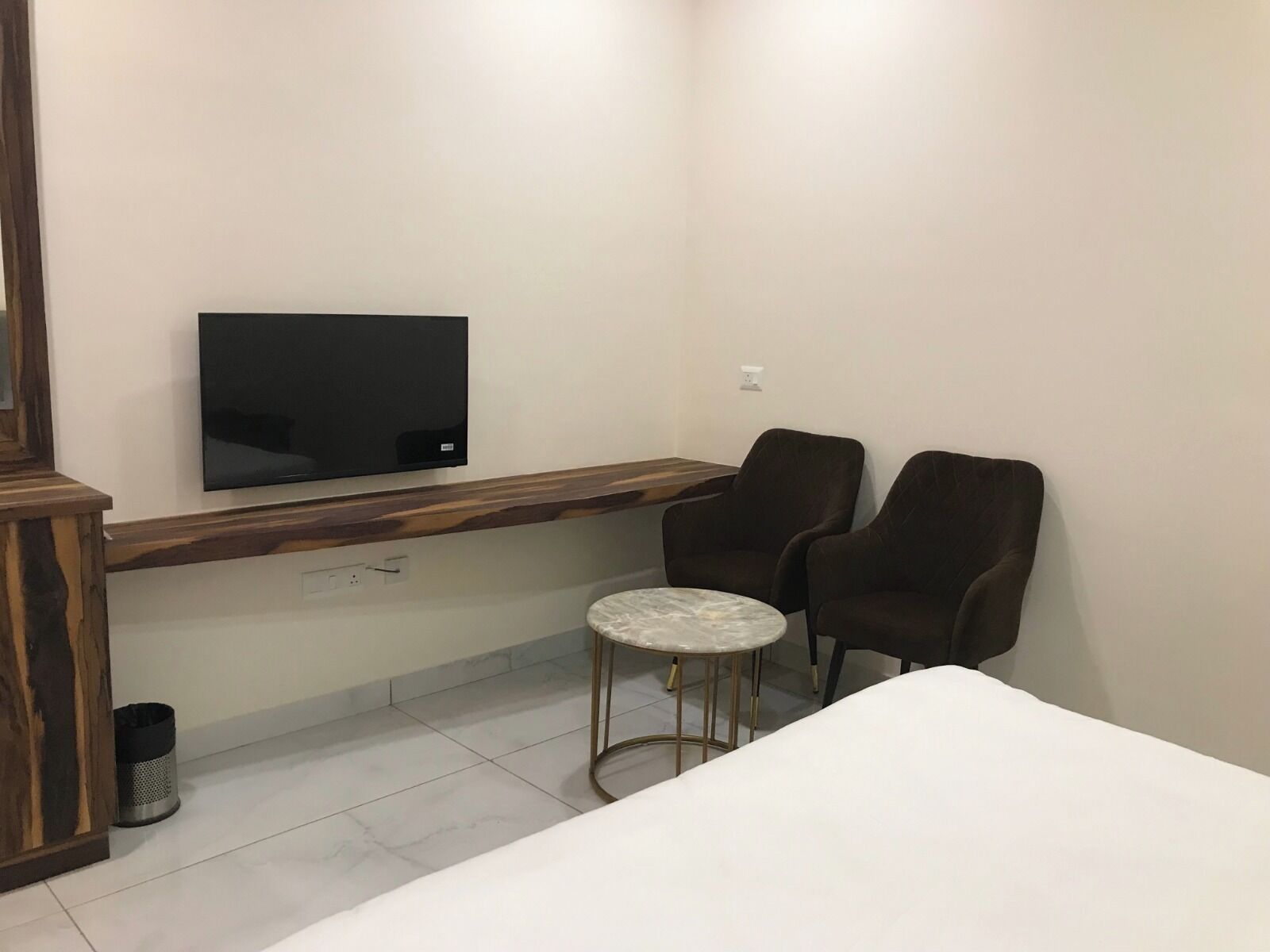 A small, modern room with a TV mounted on the wall, two chairs, a small round table, and a bed.