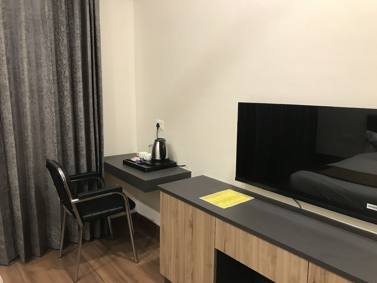 A compact hotel room with a wooden desk, a black chair, a television, and a bed.