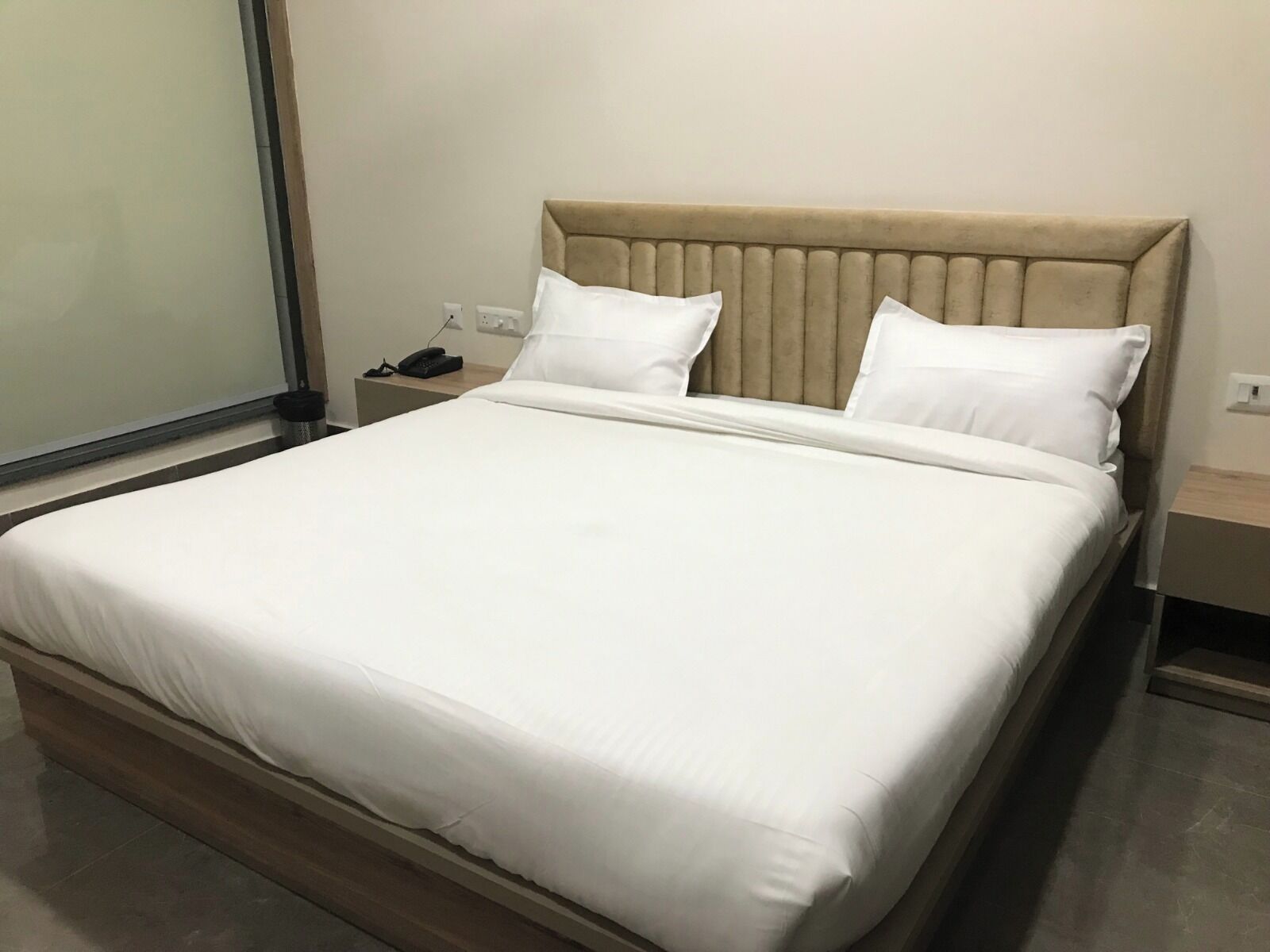 A neatly made bed with a beige headboard and white bedding in a hotel room.