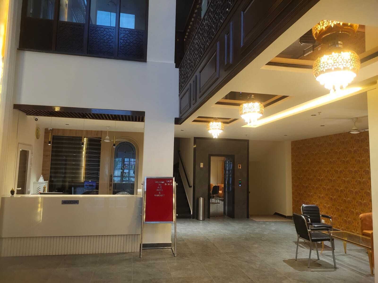 A hotel reception area with a reception desk, a red sign, and a staircase leading to an upper level.