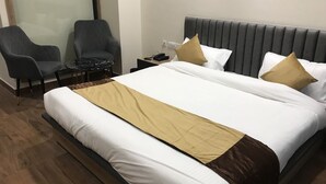 A hotel room with a large bed, two armchairs, a small table, and a nightstand with a phone. - AJ's Arcade (Pathankot)