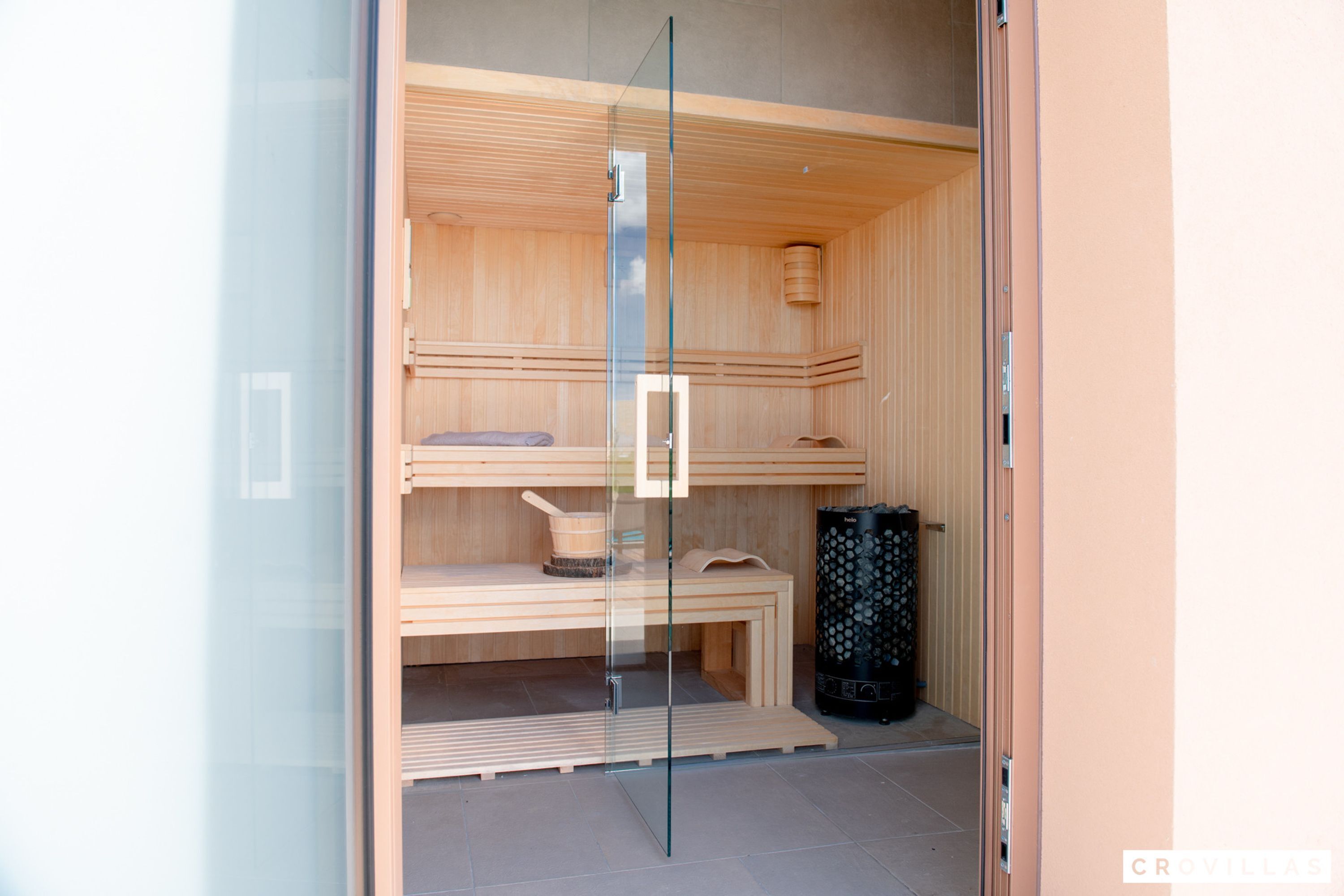 Un sauna avec des bancs en bois, une porte en verre et un appareil de chauffage noir.