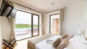 Une chambre dotée d’un grand lit, d’un téléviseur fixé au mur et offrant une vue sur une piscine extérieure et un espace patio.
