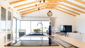 Une cuisine moderne dotée d’un grand îlot central, de poutres en bois au plafond, d’un évier intégré et d’un coin repas avec un canapé et un téléviseur.