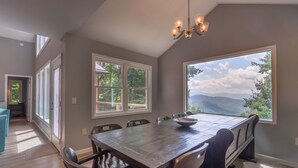 Ein Essbereich mit großem Tisch und Stühlen, einer Kandelaber und großen Fenstern mit Blick auf die Berge.