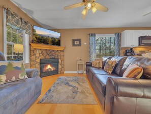 A living room with a stone fireplace, leather sofas, a rug, and a view of the outdoors. - Pool Table | Pet Friendly | Hot Tub | Arcade | WiFi (Sevierville)