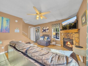 Una sala de estar con chimenea, un sofá, un televisor y un ventilador de techo.