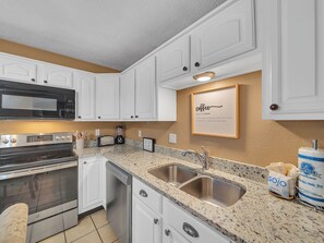 Una cocina con armarios blancos, electrodomésticos de acero inoxidable, encimera de granito y un cartel en la pared.