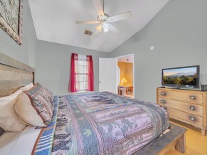 Un dormitorio con una cama, ventilador de techo, televisión y cómoda.