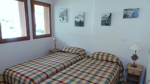 A bedroom with two beds, a nightstand, and a lamp. There are four framed pictures on the wall.