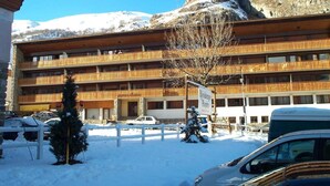 A multi-story hotel with balconies, a snow-covered parking area, and a mountainous backdrop. - Resort center, 3rd floor, balcony, parking, 53m², Valloire (Valloire)