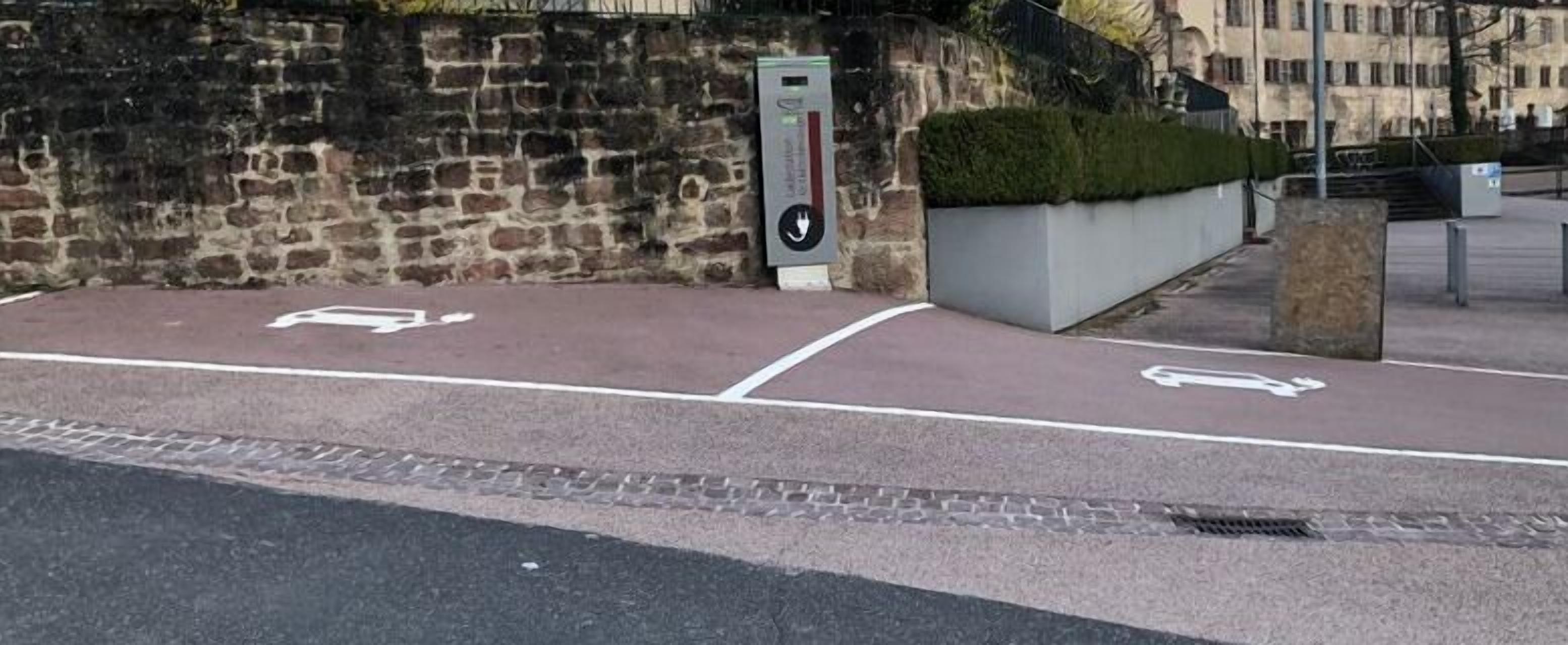 A parking area with two marked spaces for vehicles, a stone wall, and a modern electrical box.