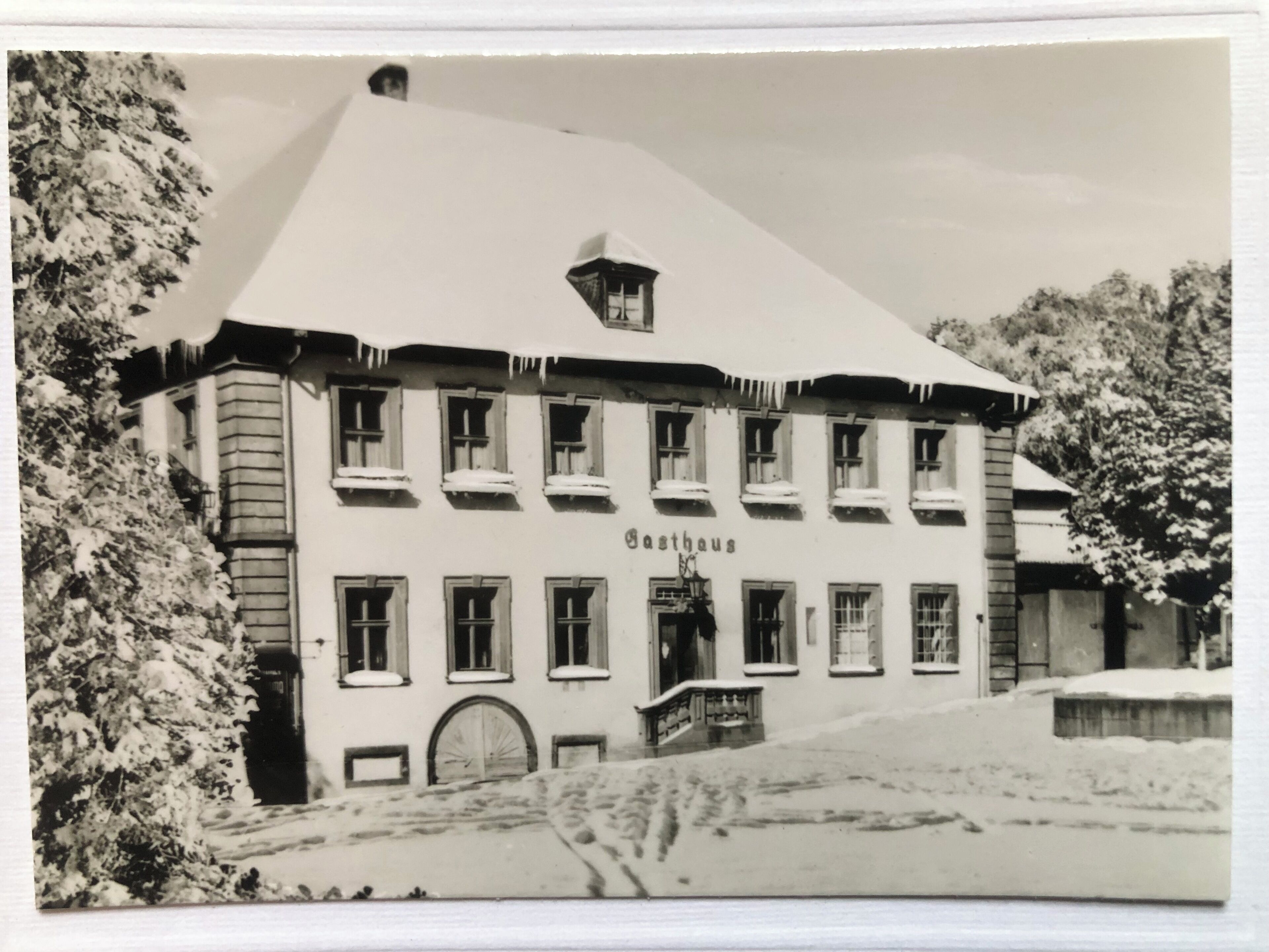 Lumipeitteinen katto ja useita ikkunoita – rakennuksessa on kyltti, jossa lukee ”Gasthaus”.