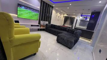 Una sala de estar moderna con un televisor de pantalla plana grande, un sillón amarillo, un sofá oscuro y piso de mármol.