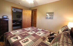 A bedroom with a quilted bedspread, a wooden door, a ceiling fan, and a framed picture on the wall.