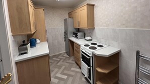 Une cuisine compacte avec des meubles en bois, un four à micro-ondes encastré, une cuisinière et un réfrigérateur.