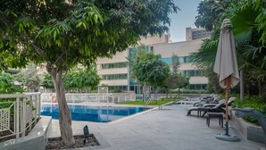 A pool area with lounge chairs, a tree, and a building in the background. - Bellavista-29BLVD Fabulous Fountain View (Dubai)