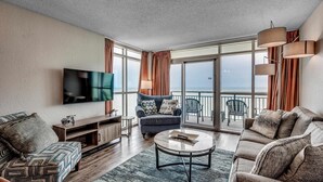 Un salon moderne doté d’un téléviseur à écran plat, d’un canapé, d’une table basse et d’un balcon offrant une vue sur la mer.