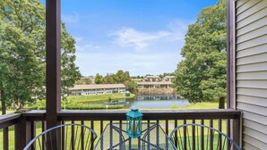 A covered outdoor area with a table and chairs, overlooking a lake and buildings in the background. - Pointe Royale Getaway – ‘Fore’ 4 (Branson)
