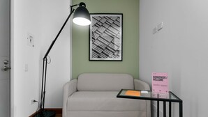 Une pièce comprenant un canapé, un lampadaire, une œuvre d’art abstraite encadrée et un panneau d’accueil posé sur une table en verre.