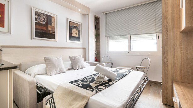 A modern bedroom with a bed, bedside tables, a window with blinds, and artwork on the walls. - Unik Vacation Zamenhoff (Tarragona)