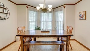 A dining room with a wooden table, chairs, a chandelier, and large windows with sheer curtains. - Southall Cottage: 3bd*Serene Outdoor Space* (Franklin)