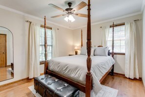 Une chambre à coucher avec un lit à baldaquin, un ventilateur de plafond, une table de chevet, une lampe et une fenêtre avec des rideaux.