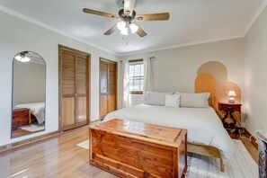Quarto com cama, piso de madeira, ventoinha no teto e mesa de cabeceira com abajur.