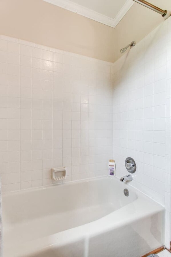 A bathroom with white tiles, a bathtub, a handheld showerhead, and a soap dispenser.