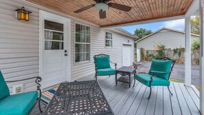 A covered porch with a ceiling fan, two chairs with teal cushions, a small table, and a lantern. - Clean 3BR · Quiet Block · Backyard with Hoop (Spring Hill)
