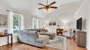 A spacious living room with a sectional sofa, a ceiling fan, a television, and a fireplace. - Clean 3BR · Quiet Block · Backyard with Hoop (Spring Hill)