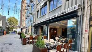 An outdoor seating area with tables and chairs, a planter box with greenery, and a building with a sign reading "PERA PORT LOUNGE". - The Port Palace Otel (Istanbul)