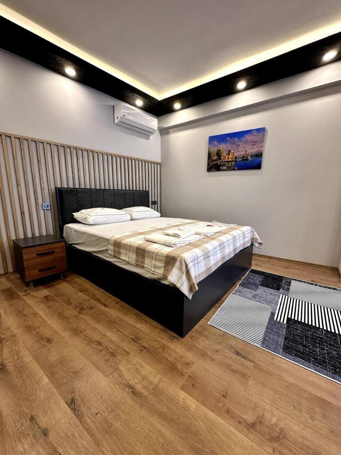 Un dormitorio moderno con cama, mesita de noche y un cuadro en la pared.