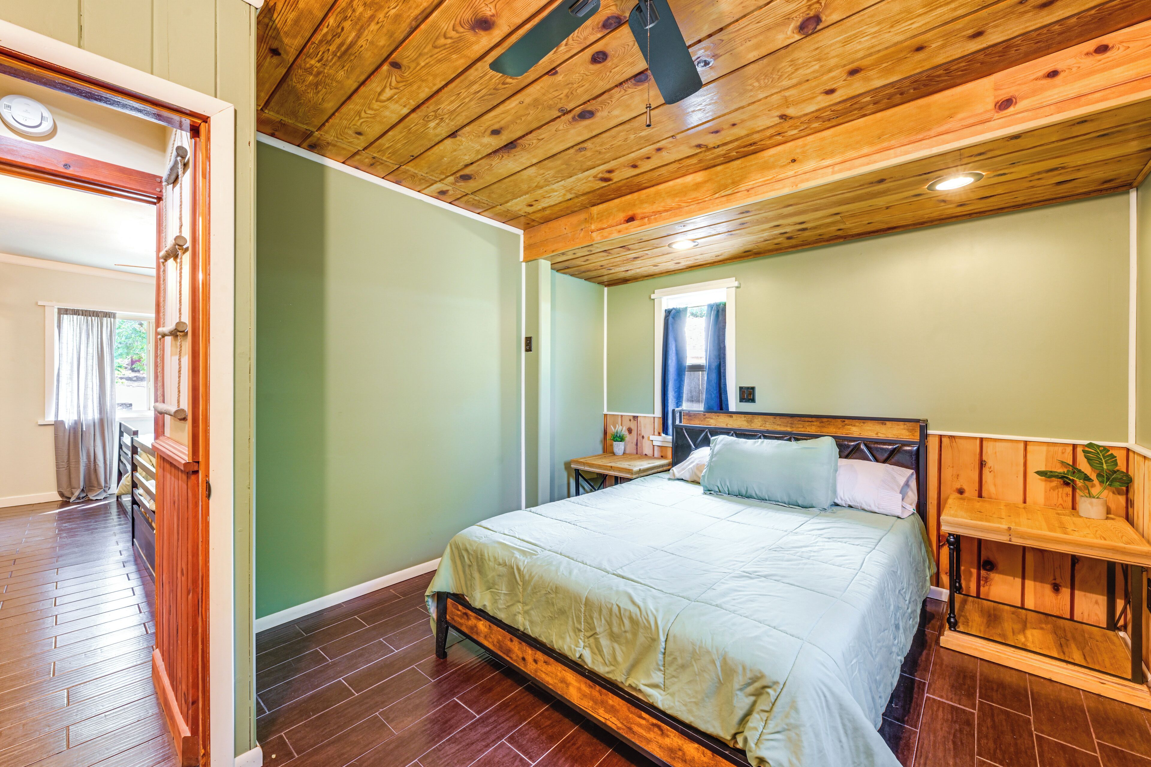 Un dormitorio con estructura de cama de madera, una mesita de noche y una ventana con cortinas.