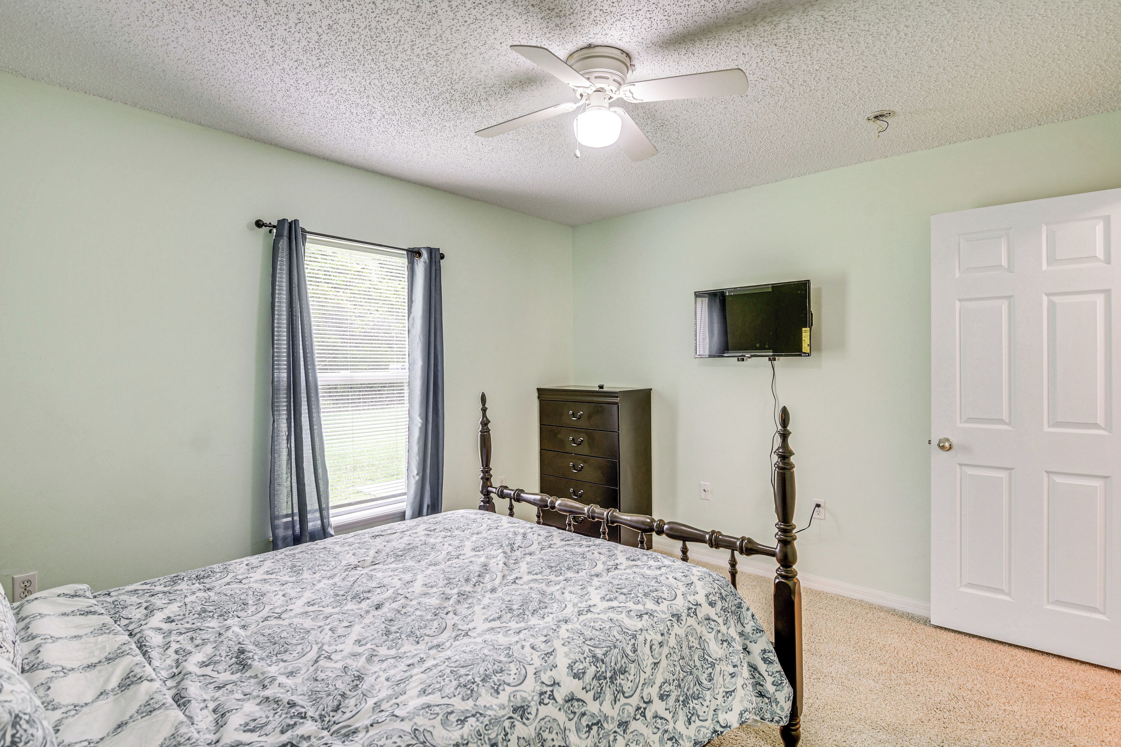 A bedroom with a bed, a ceiling fan, a dresser, a television, and a door.