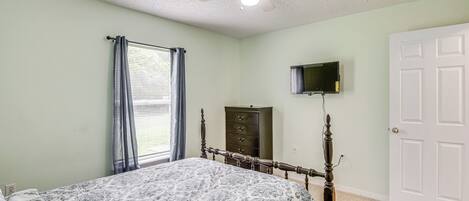 A bedroom with a bed, a ceiling fan, a dresser, a television, and a door.
