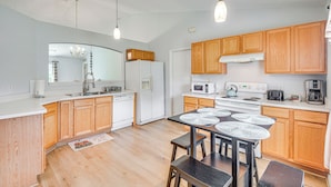 Una cocina moderna con gabinetes de madera, un refrigerador blanco, una estufa y un comedor con una mesa y sillas.