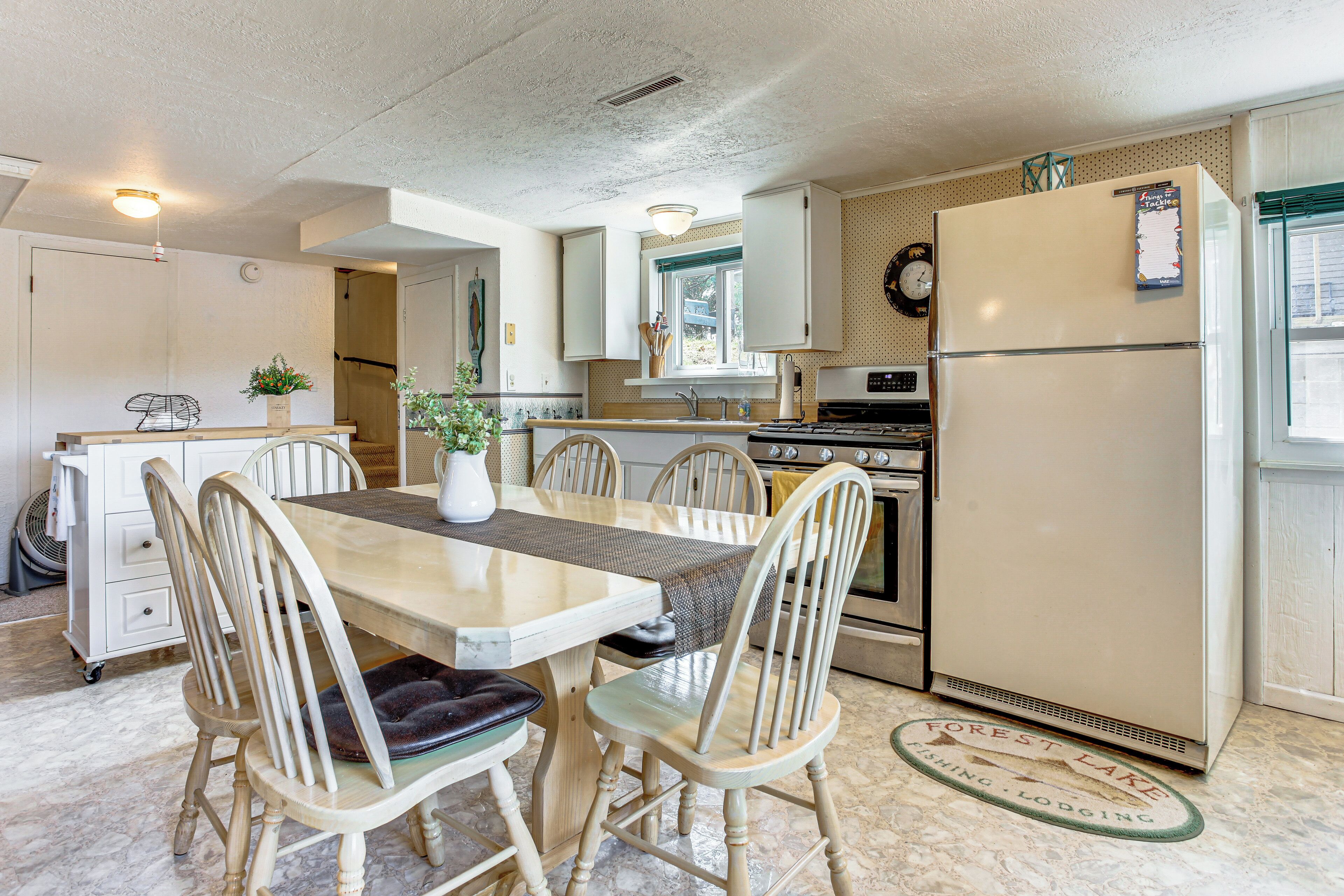 Una cocina compacta con una mesa de comedor, sillas, un refrigerador y un reloj en la pared.