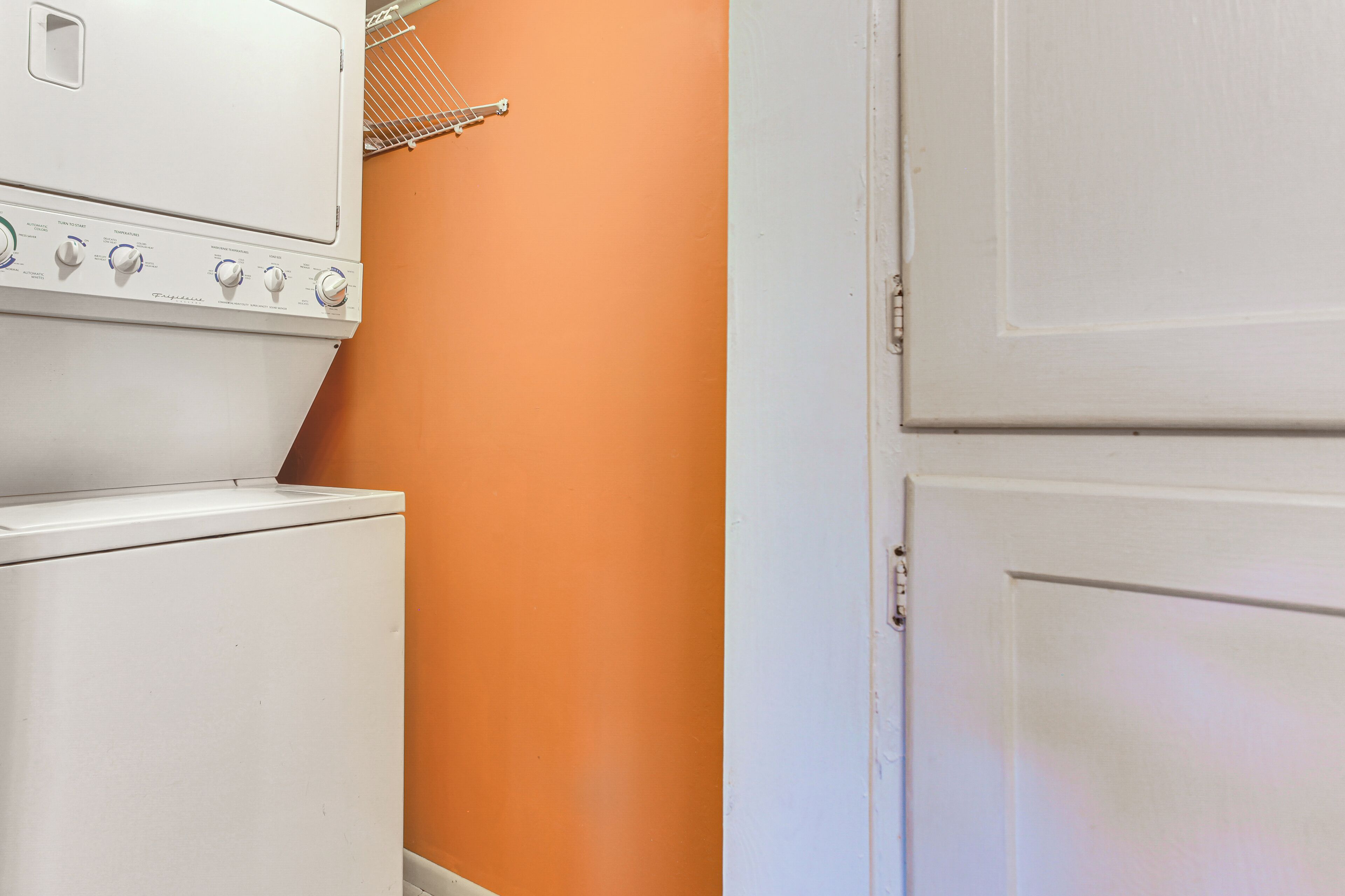 A laundry area with a white washing machine and dryer, an orange wall, and a white door.