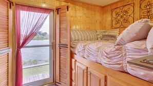 A wooden cabin interior with a bed, a window with curtains, and a decorative wall piece. - 'Da Boat House' w/ World-class Bayou Fishing! (Houma)