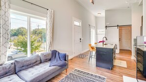 A modern living room with a grey sofa, a kitchen area with a black island, and a dining space with wooden chairs. - 3 Mi to Duke: Downtown Durham Cottage! (Durham)