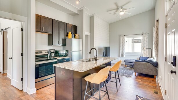 A modern kitchen with a central island, bar stools, and a dining area with a sofa and chairs. - 3 Mi to Duke: Downtown Durham Cottage! (Durham)