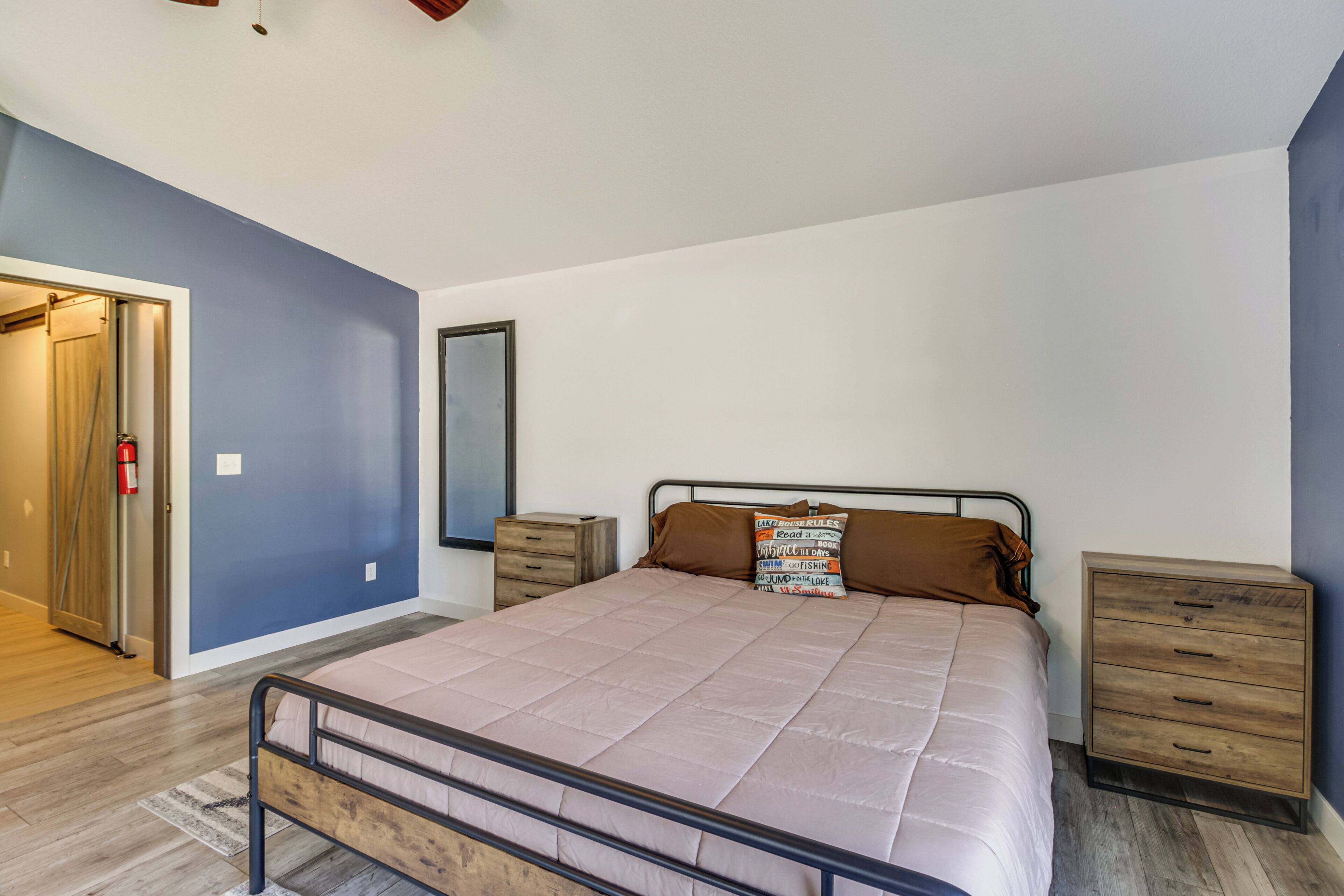A bedroom with a bed, wooden nightstands, a dresser, and a door leading to another room.