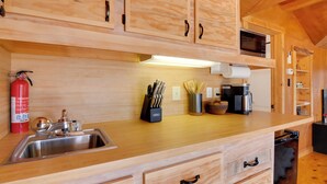 Una cucina in legno con lavello in acciaio inossidabile, estintore, portacoltelli, macchina da caffè e forno a microonde.