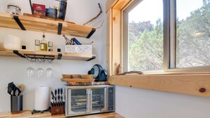Una cocina con estantes de madera, horno tostador y ventana con vista a árboles.