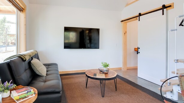 Una sala de estar moderna con un sofá de cuero negro, una mesa redonda de madera con una planta, y un televisor de pantalla plana montado en la pared.