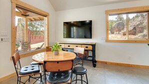 Un coin repas avec une table et des chaises en bois, une plante en pot et un téléviseur fixé au mur.