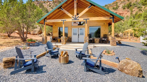 Un chalet avec une façade en bois, un toit végétalisé et un patio aménagé avec des fauteuils Adirondack et un foyer.