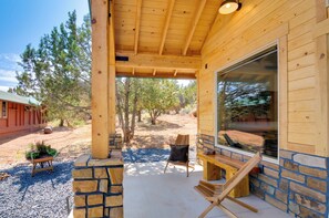 Una cabaña de madera con porche cubierto, paredes de piedra y un ventanal grande.