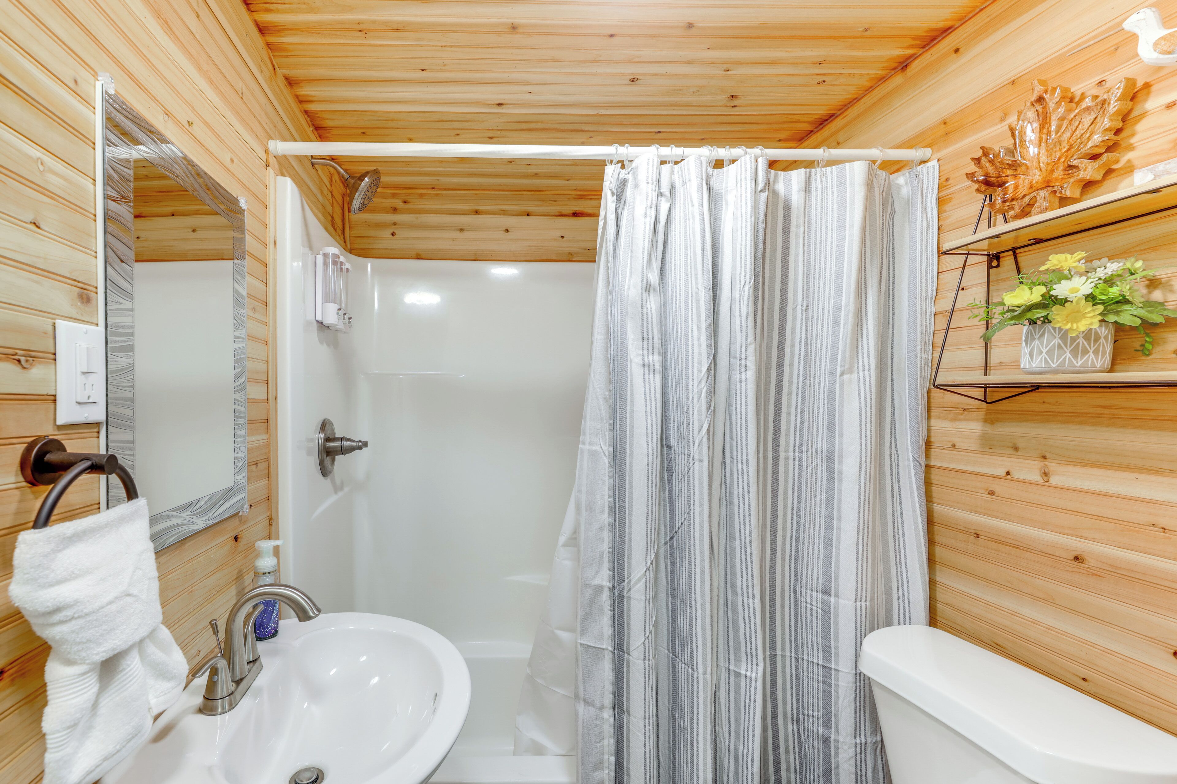Une salle de bain aux murs lambrissés, équipée d’une douche, d’un lavabo et de toilettes.